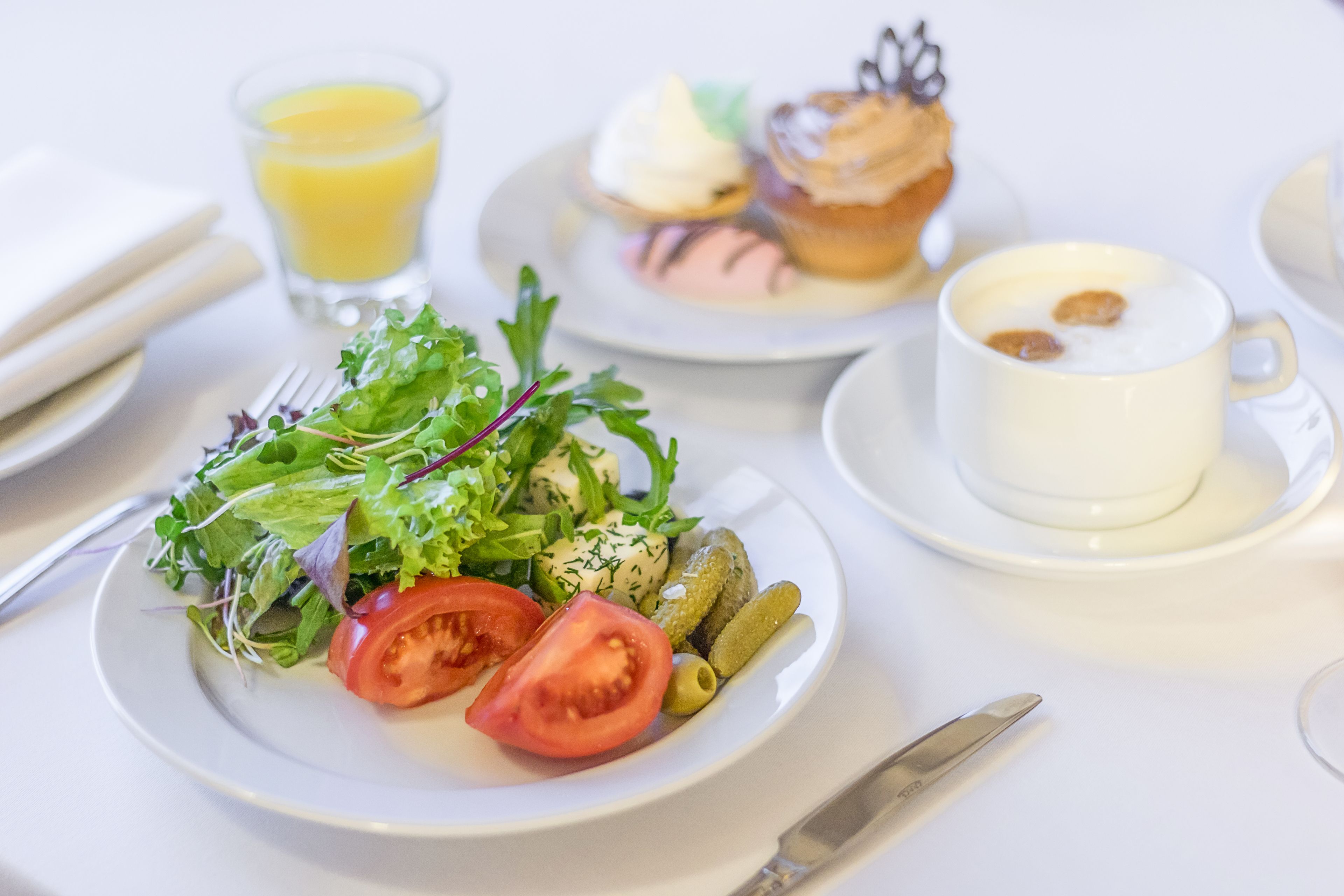 A table with a plate of salad, a muffin, a cup of coffee, and a glass of orange juice.