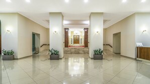 Un vestíbulo amplio con una escalera central, plantas en macetas y un mostrador de recepción.