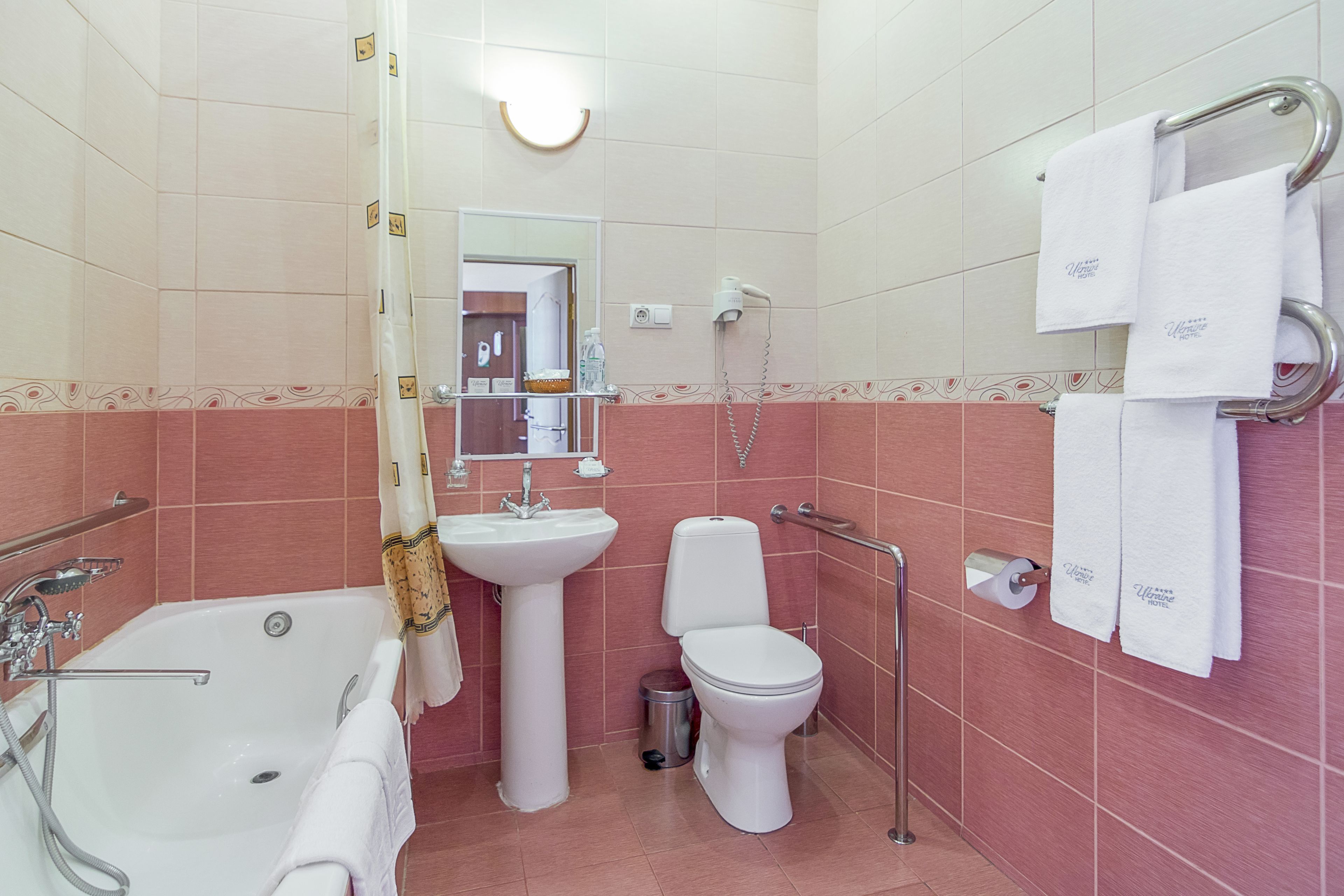 A bathroom with a bathtub, sink, toilet, and handrails.