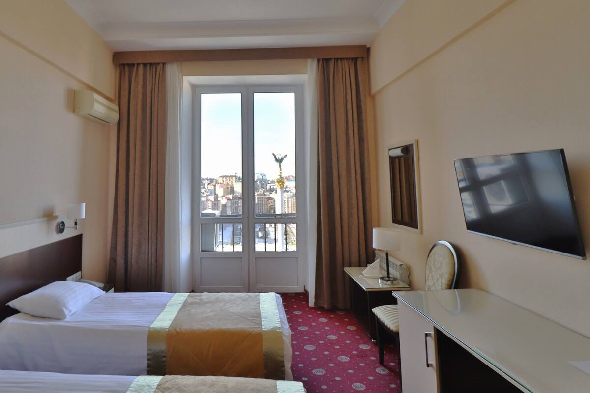Una habitación de hotel con dos camas, un escritorio, un televisor y una ventana con cortinas.