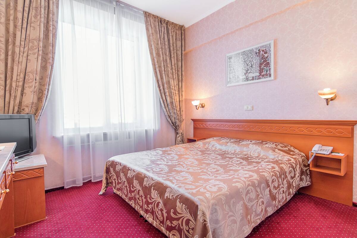 Habitación de hotel con una cama grande, un televisor sobre una cómoda de madera, un escritorio y un teléfono instalado en la pared.