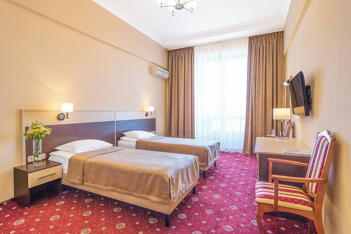 Habitación de hotel con dos camas, un escritorio, una silla, un televisor y una ventana con cortinas.