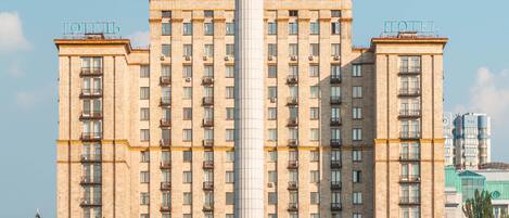 A large hotel building with a central column and a statue on top.