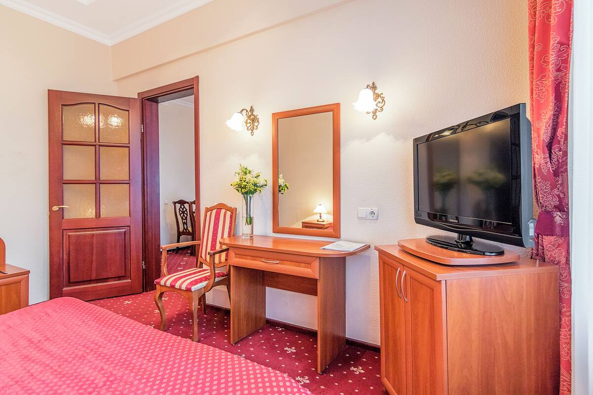 Una habitación de hotel con cama, escritorio, silla, televisor y espejo.