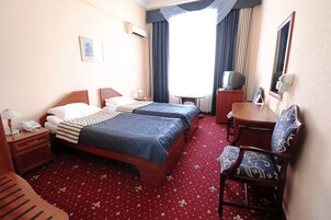 Hotelkamer met twee bedden, een bureau, een stoel, een televisie, een telefoon en een raam met gordijnen.