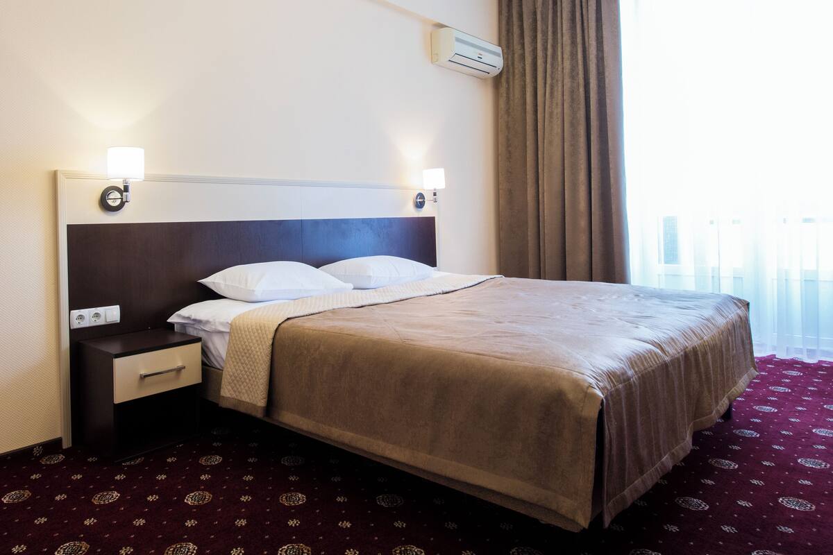 Una habitación de hotel con cama, mesita de noche, lámpara y aire acondicionado.