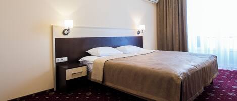 Una habitación de hotel con cama, mesita de noche, lámpara y aire acondicionado.