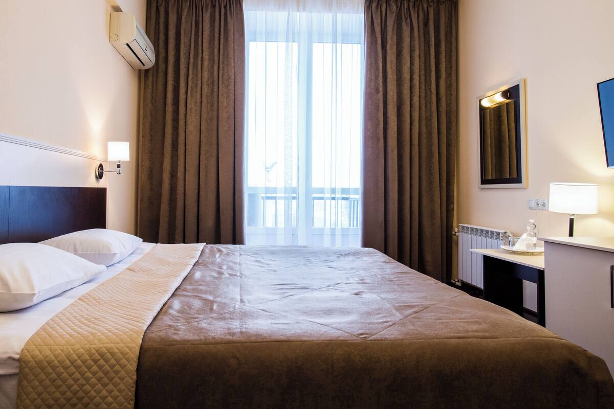 Una habitación de hotel con cama, mesita de noche, espejo y ventana con cortinas.