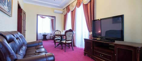 Una sala de estar con sofá de cuero, un televisor sobre un mueble de madera, un comedor con mesa y sillas, y una araña.