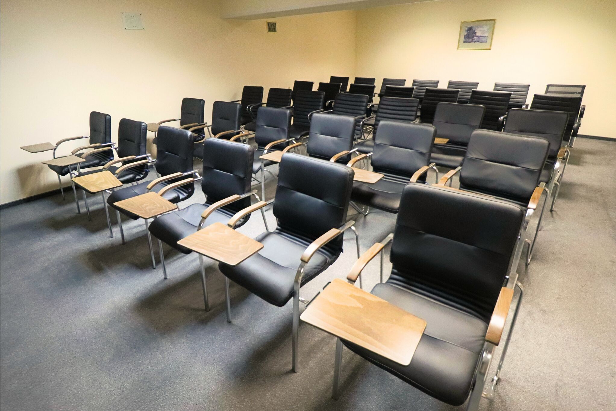 A classroom with rows of black chairs and wooden desks, arranged in a classroom setting.