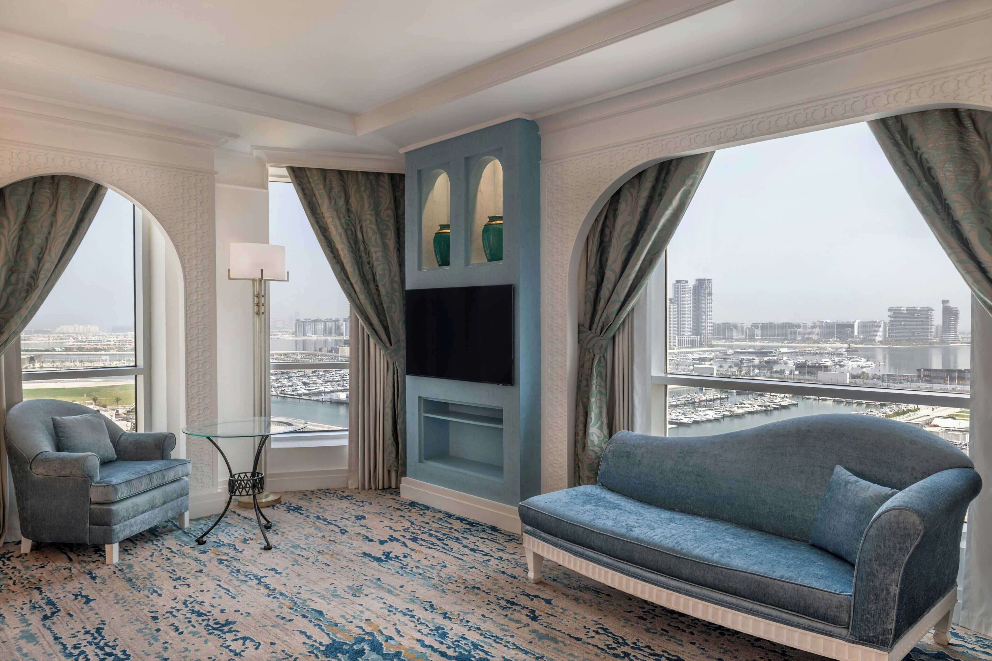 Ein modernes Hotelzimmer mit großem Fenster, einer Couch, einem Sessel, einem Fernseher und einer dekorativen Wandverkleidung.