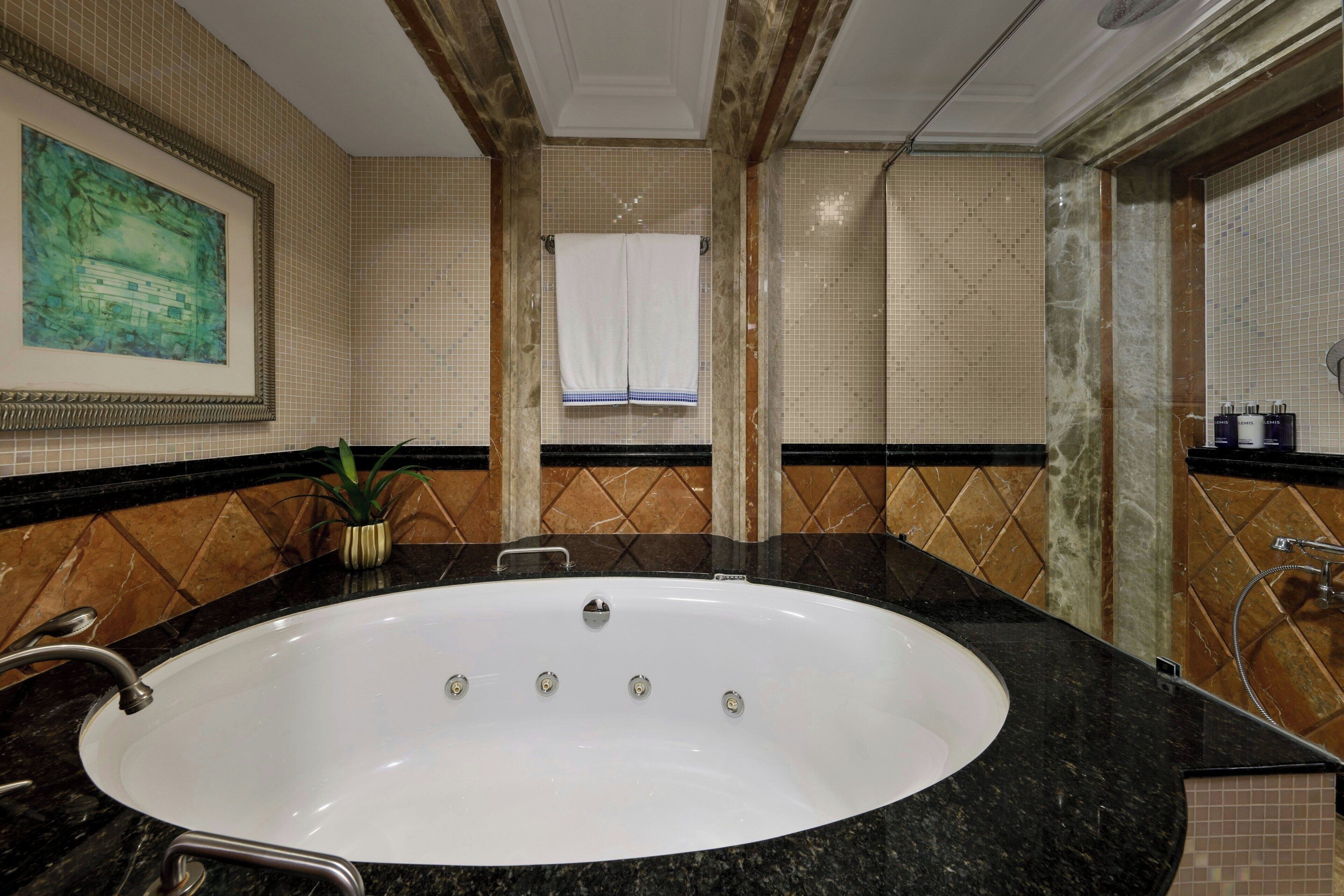 A bathroom with a large oval sink, a framed painting on the wall, and a window with a towel hanging.