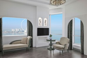 A spacious room with a large window offering a view of the sea and a Ferris wheel. There are two upholstered chairs and a small table with a plant. - Al Habtoor Grand Resort, Autograph Collection® (Dubai)