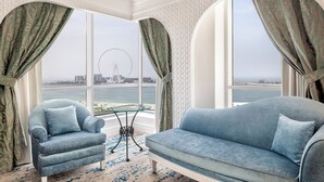 A room with a sofa and armchair facing a large window with a view of a Ferris wheel and a bridge. - Al Habtoor Grand Resort, Autograph Collection® (Dubai)