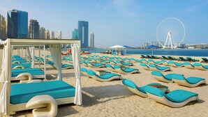 A beach with rows of sunbeds and a canopy structure, a Ferris wheel in the background, and a city skyline across the water. - Al Habtoor Grand Resort, Autograph Collection® (Dubai)