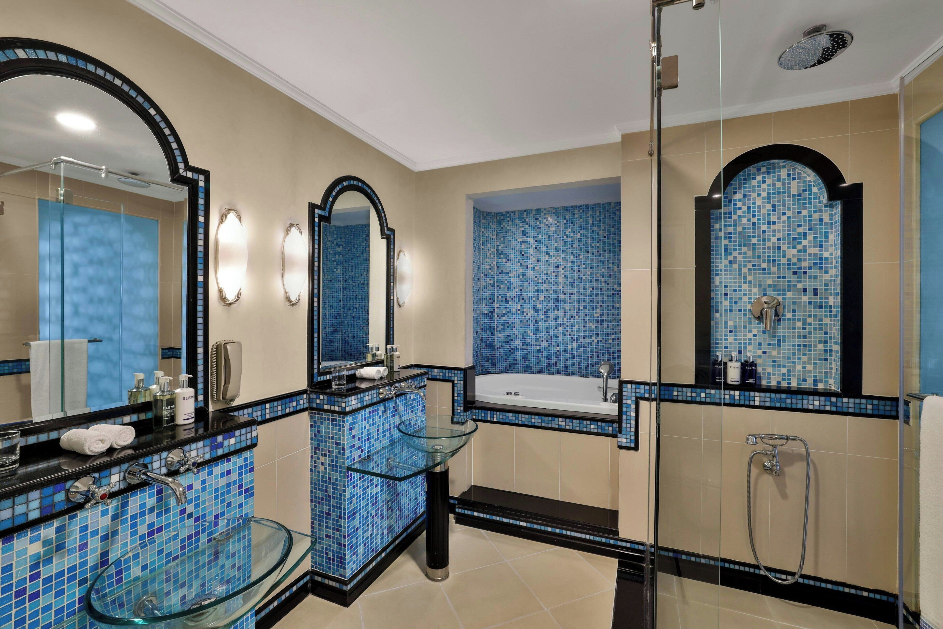 Une salle de bain moderne dotée d’une douche à parois de verre, d’un lavabo en verre et d’une baignoire dont les murs sont recouverts de mosaïques.
