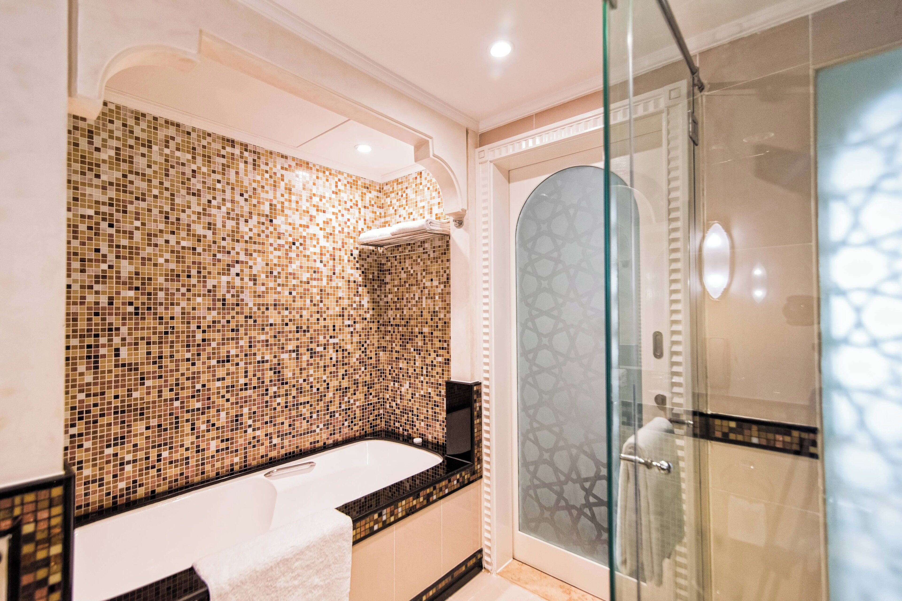 A modern bathroom with a mosaic tile wall, a freestanding bathtub, and a glass-enclosed shower area.