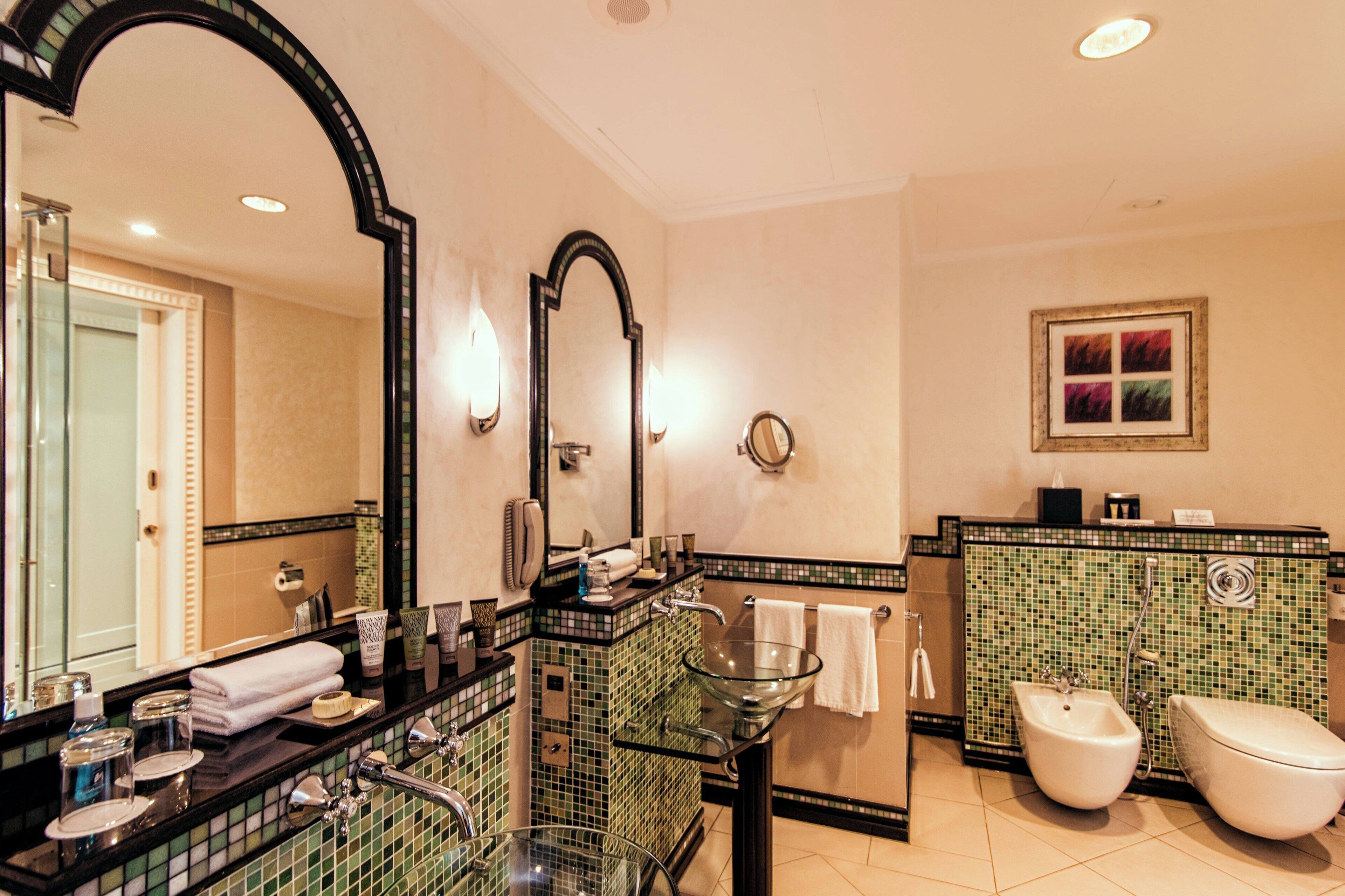 A modern bathroom with a glass sink, a large mirror, a bidet, and a tiled backsplash.