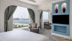 Habitación de hotel con una cama grande, dos sillones, un televisor y vistas a una noria.