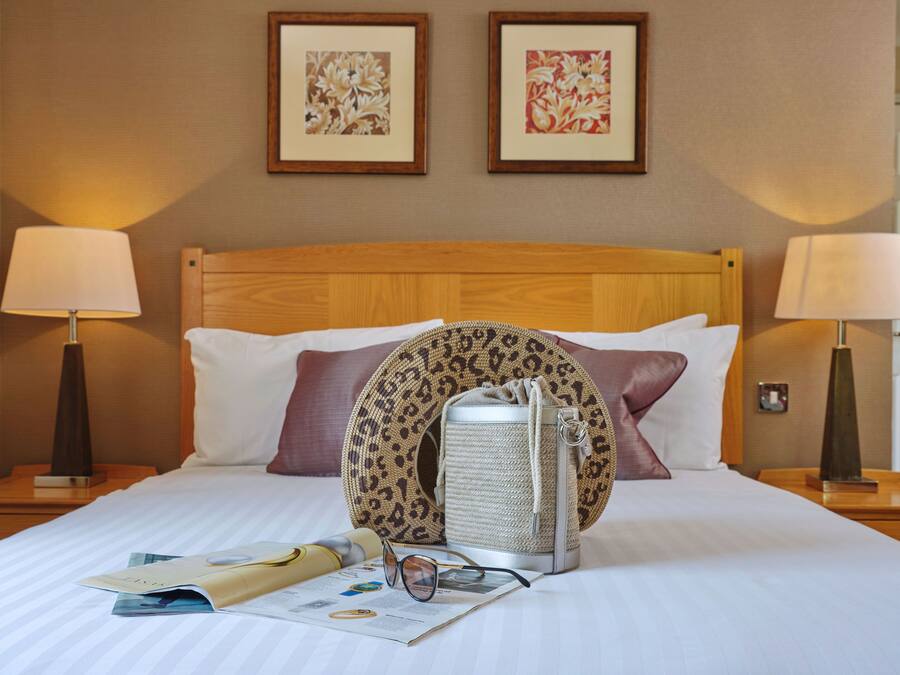 Una habitación de hotel con una cama, dos lámparas, un cabecero y dos cuadros en la pared.