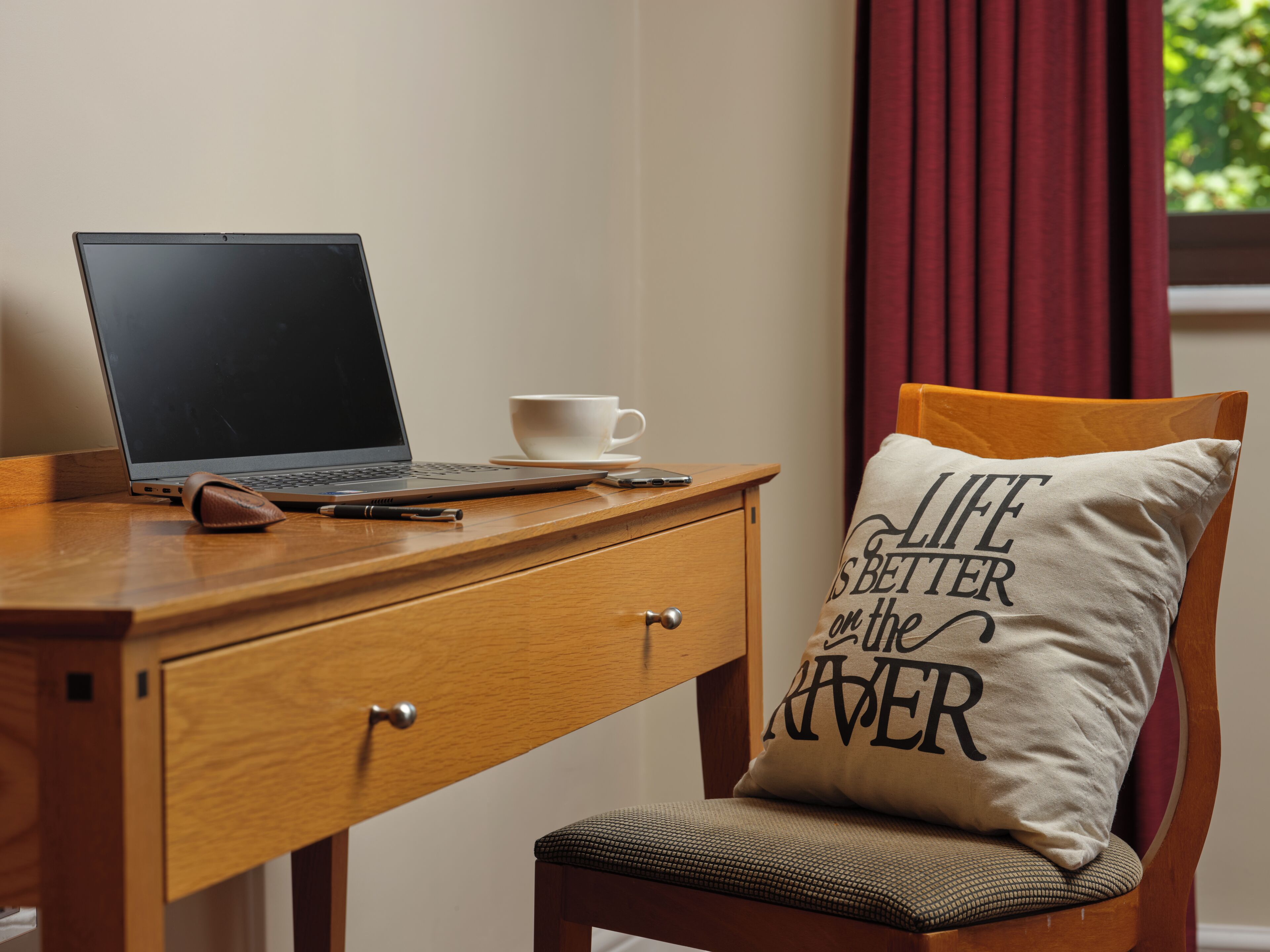A wooden desk with a laptop, a white cup, and a cushion with text.