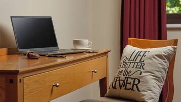 A wooden desk with a laptop, a white cup, and a cushion with text.