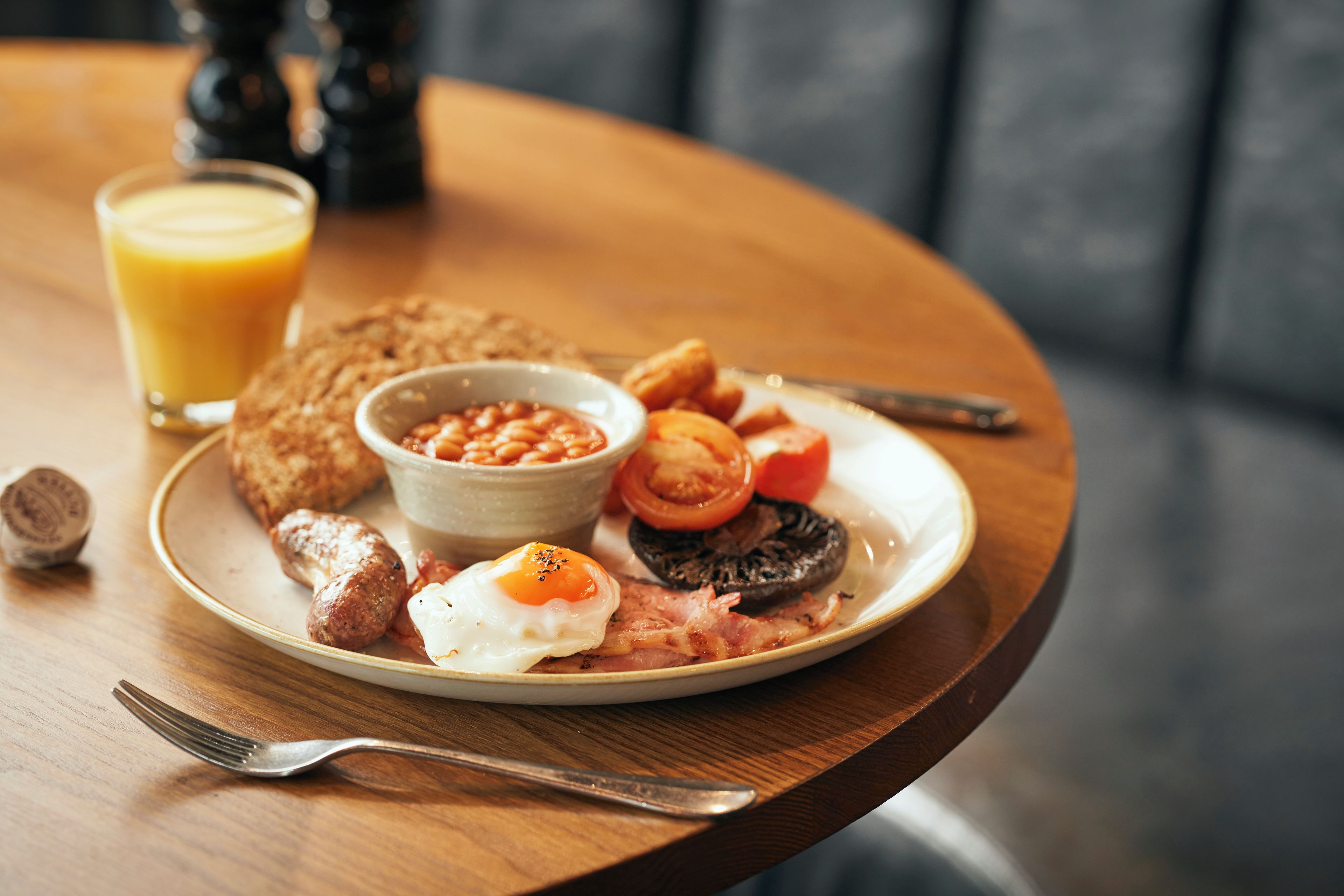 A plate of breakfast food including eggs, bacon, tomatoes, beans, and toast, with a glass of orange juice on the side.