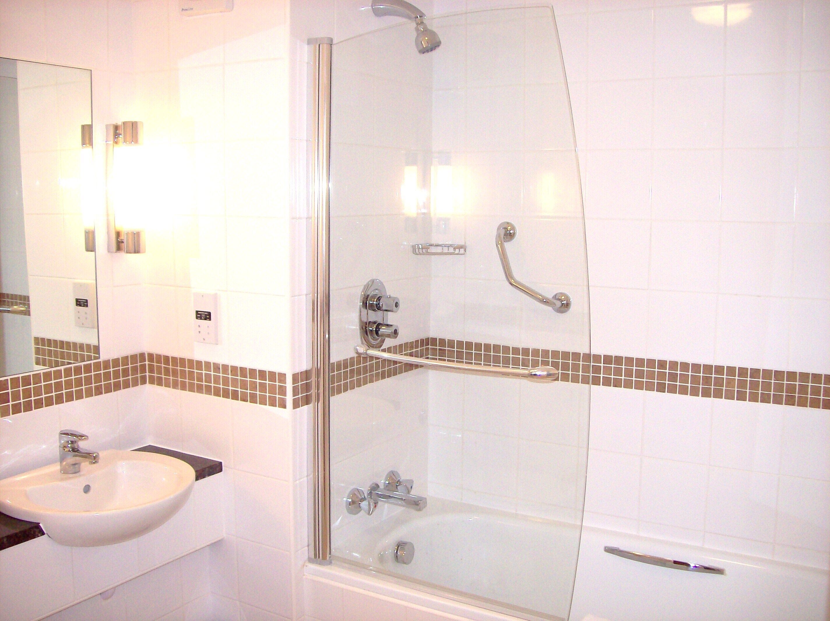 Un baño con ducha envuelta en cristal, un lavamanos y un espejo.