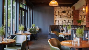 En restaurang med avskilda sittplatser i bås och vid bord, krukväxter och inramade botaniska illustrationer på väggen.