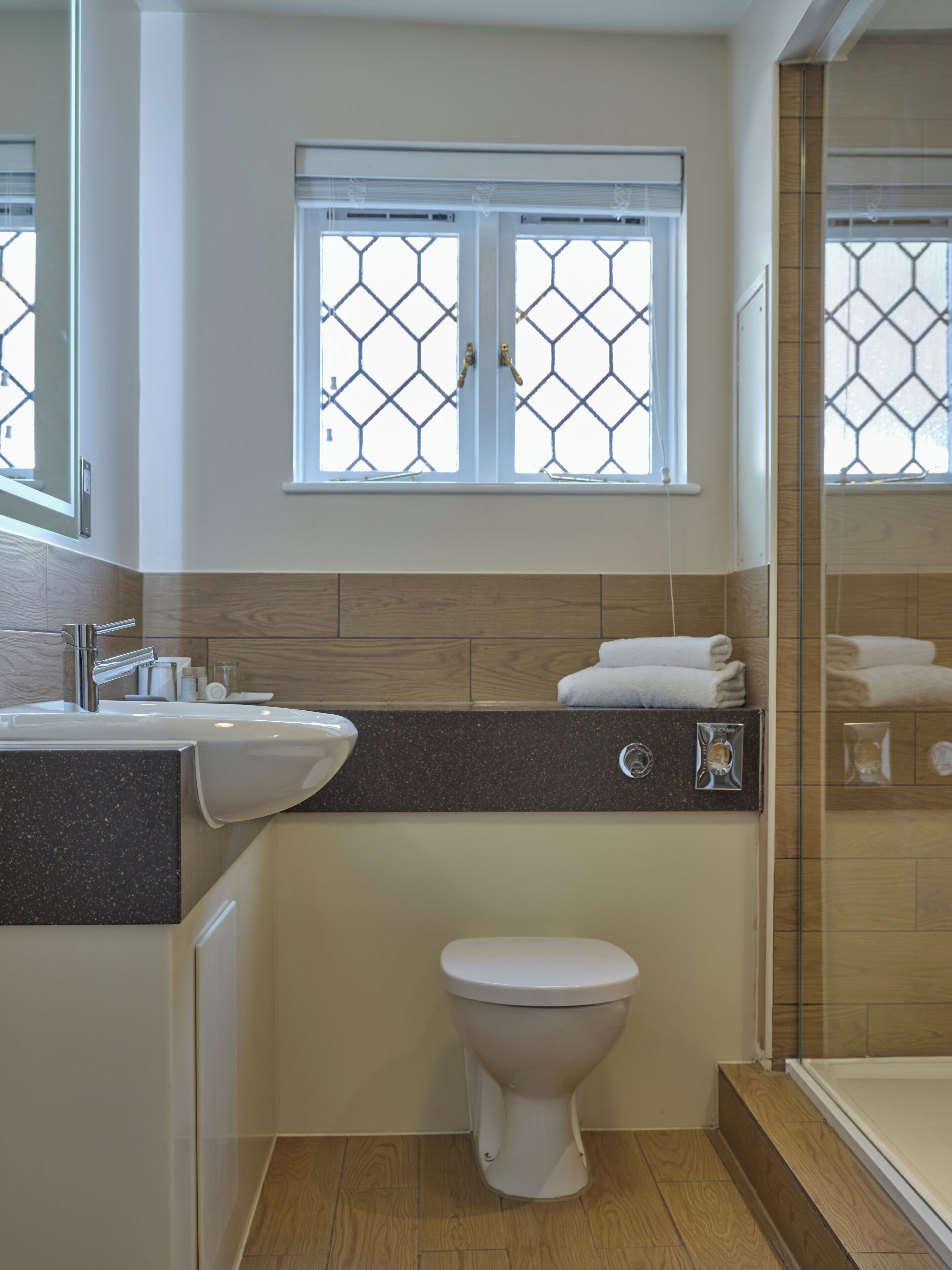 A bathroom with a sink, toilet, and window with a geometric pattern.