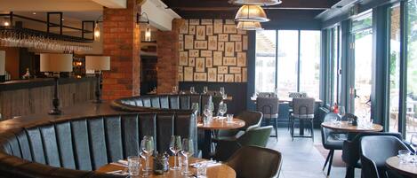 A restaurant interior with a curved bar, leather booths, and a wall of framed botanical prints.