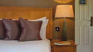 Una cama bien hecha con almohadas marrones y blancas, una lámpara de noche y una mesita de noche de madera con un libro.