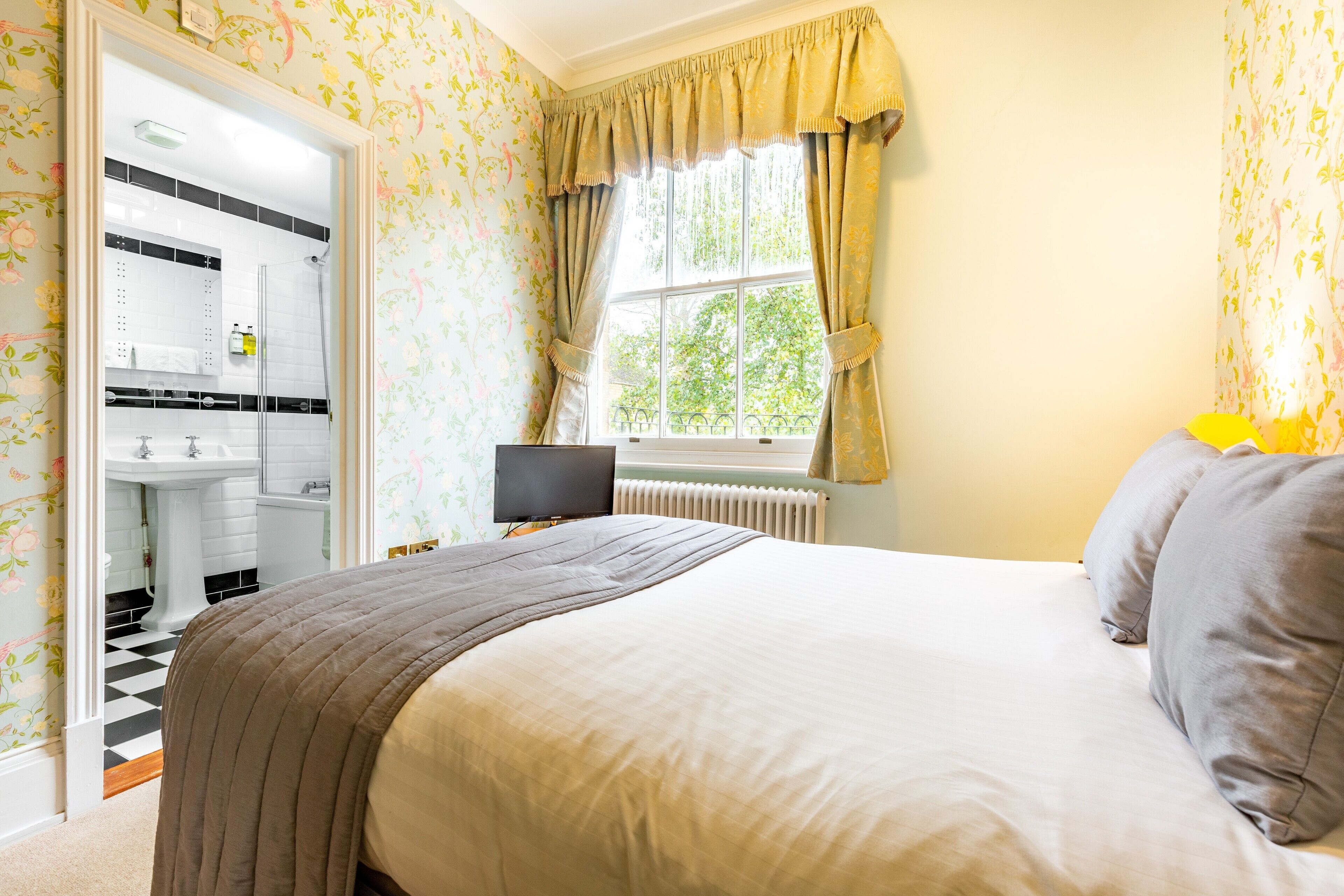 Une chambre à coucher avec un lit, une télévision et une fenêtre avec des rideaux.