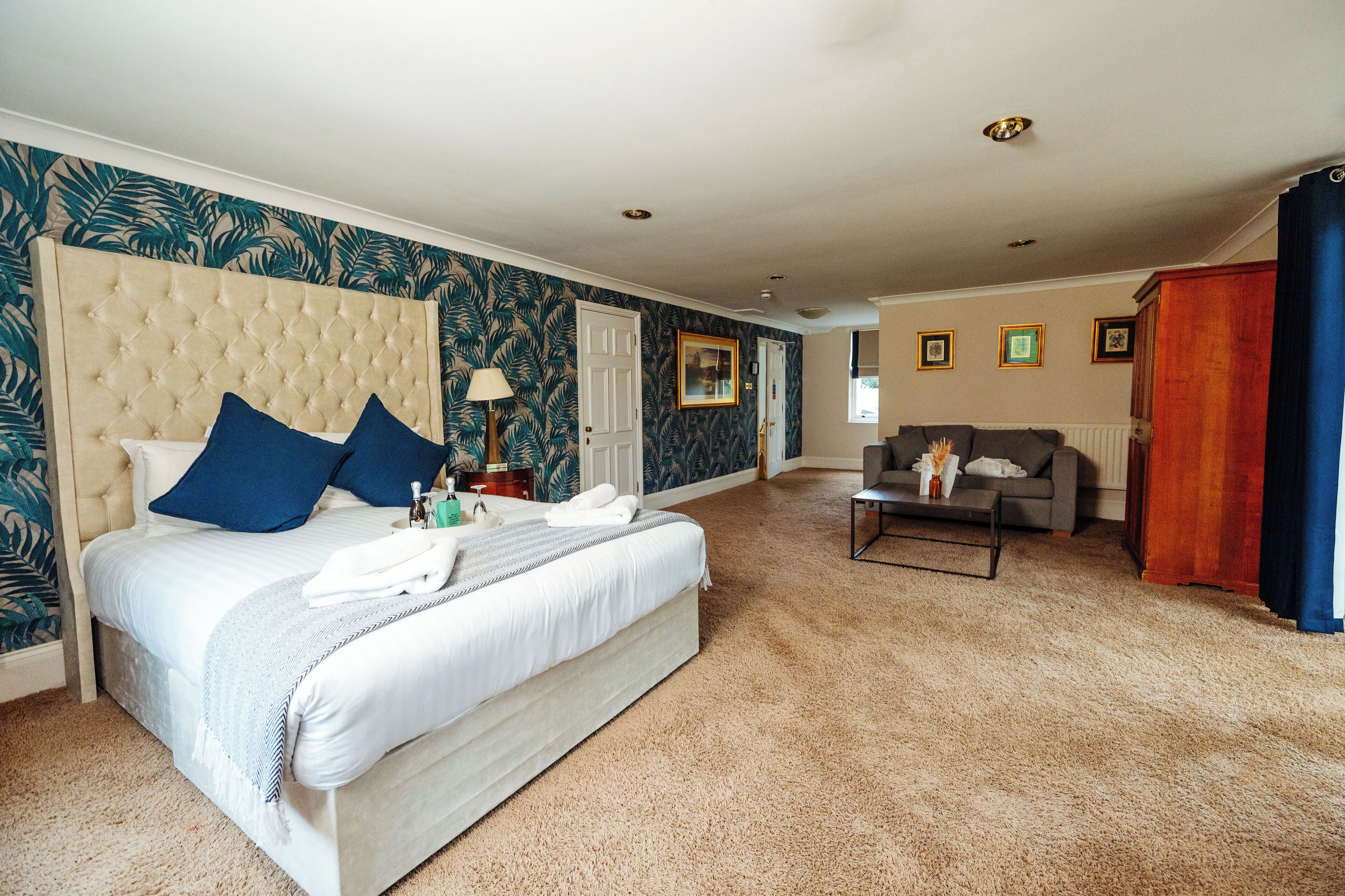 A hotel room with a large bed, a sofa, a coffee table, and a door leading to another room.