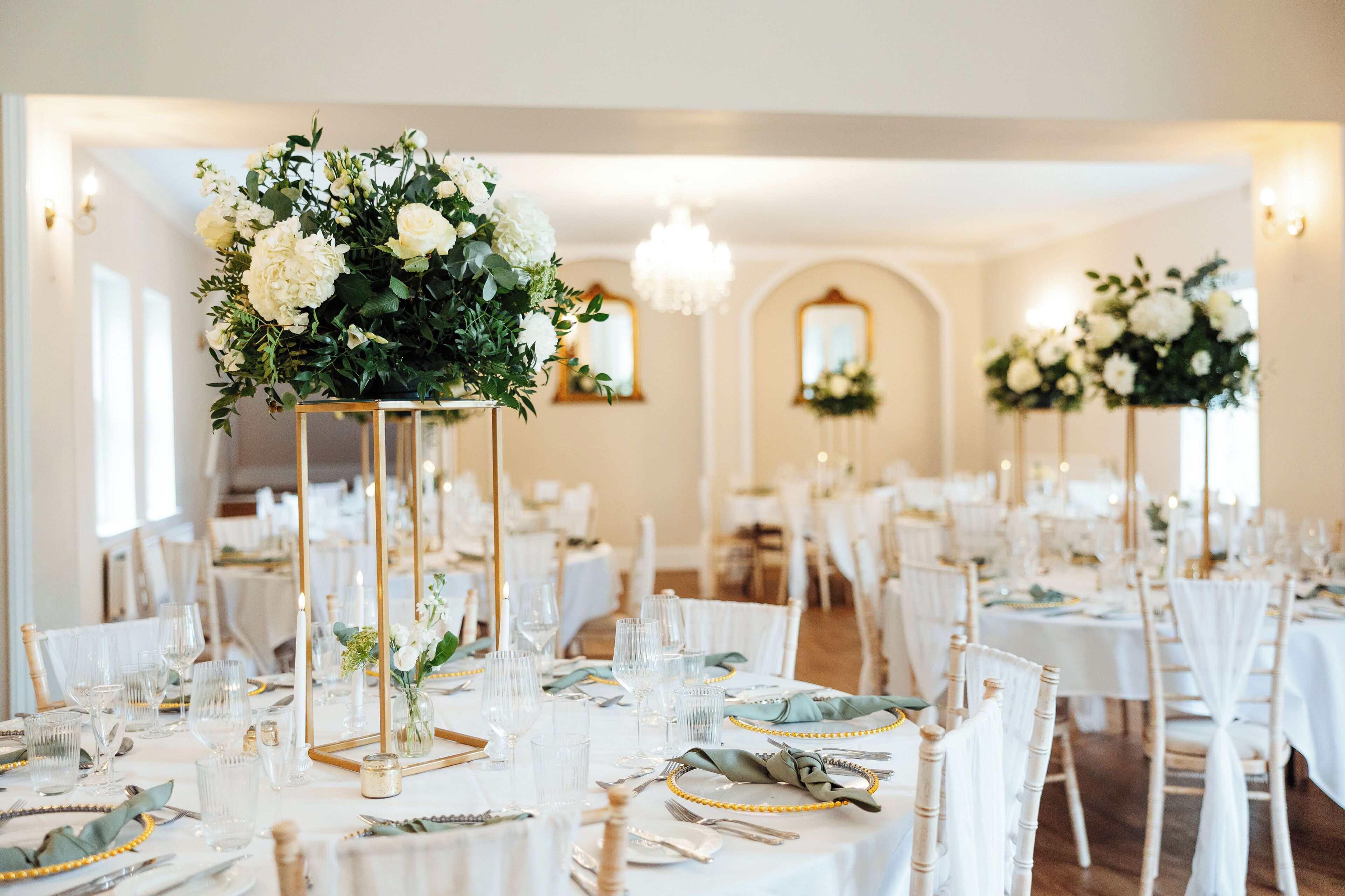 A banquet hall with round tables set for a formal event, featuring floral centerpieces and elegant table settings.