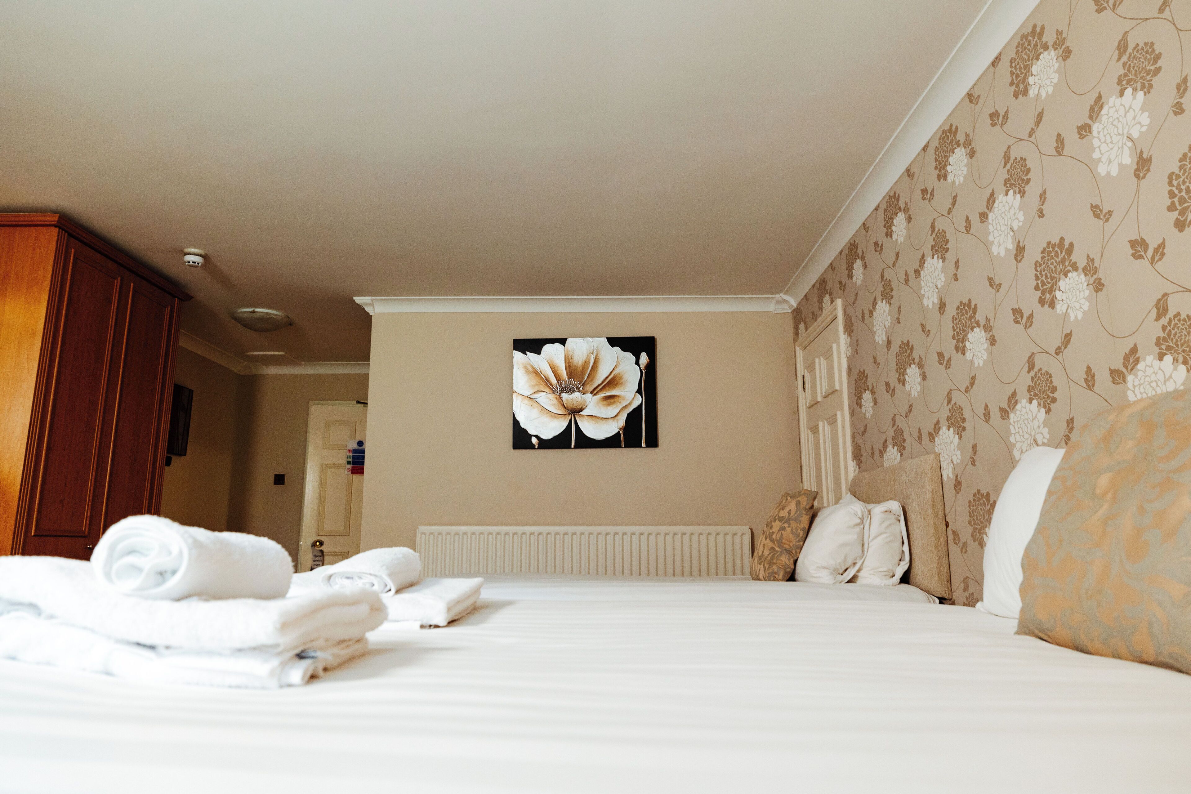 A hotel room with a bed, towels, a floral wall design, and a large flower painting.
