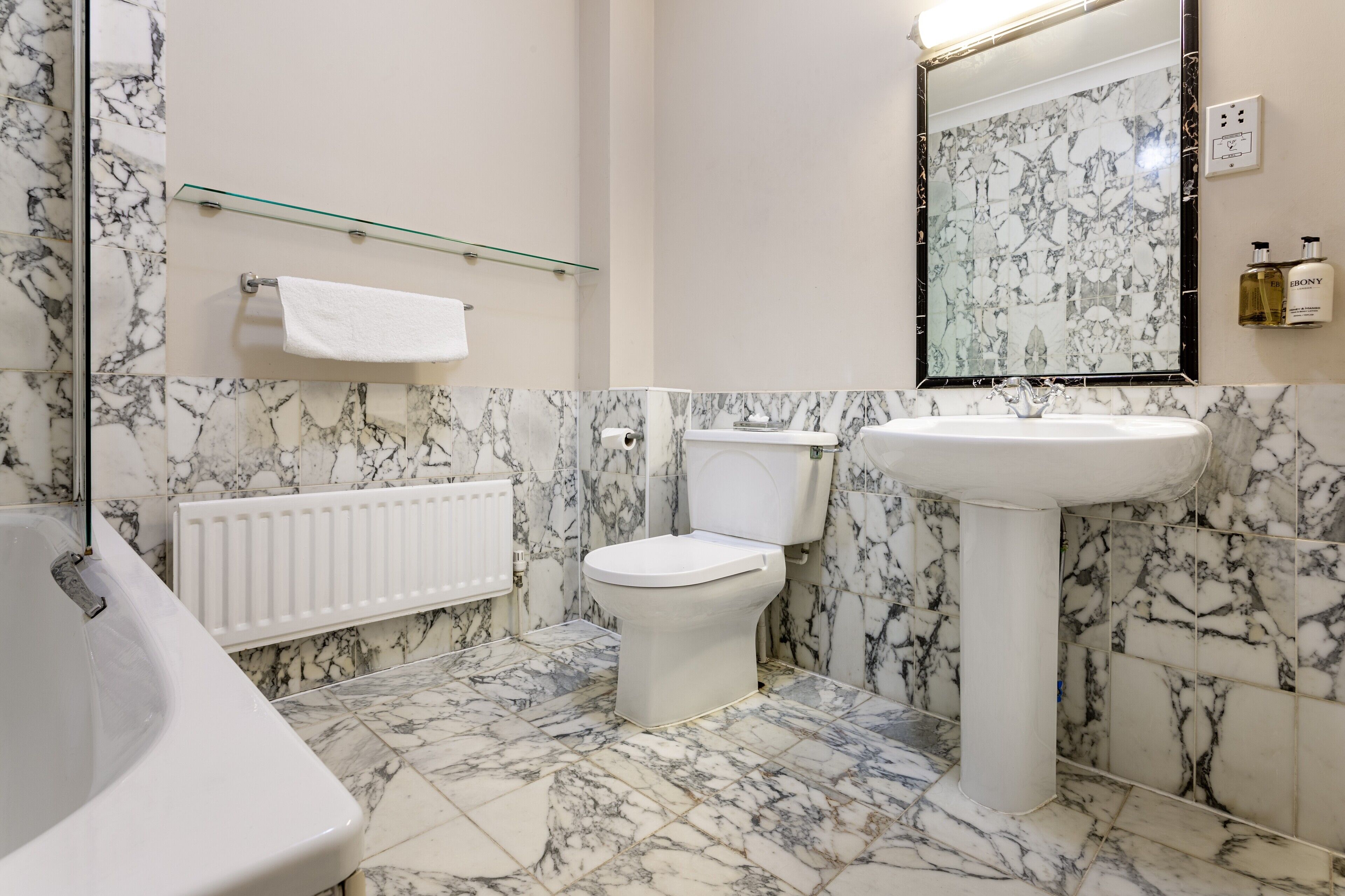 A bathroom with a marble floor, a white bathtub, a toilet, and a sink.
