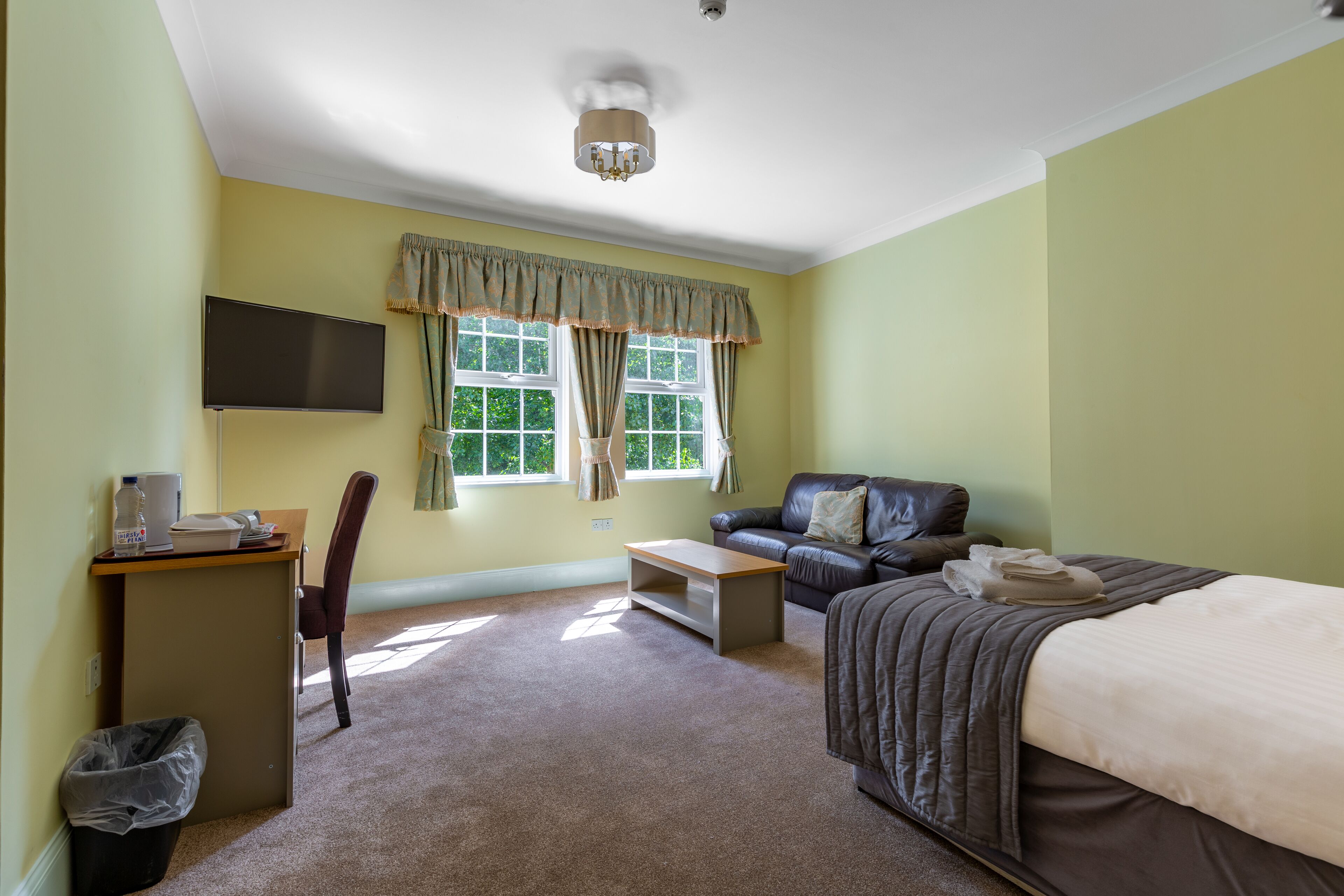 A hotel room with a bed, a desk, a chair, a sofa, a TV, and a window with curtains.