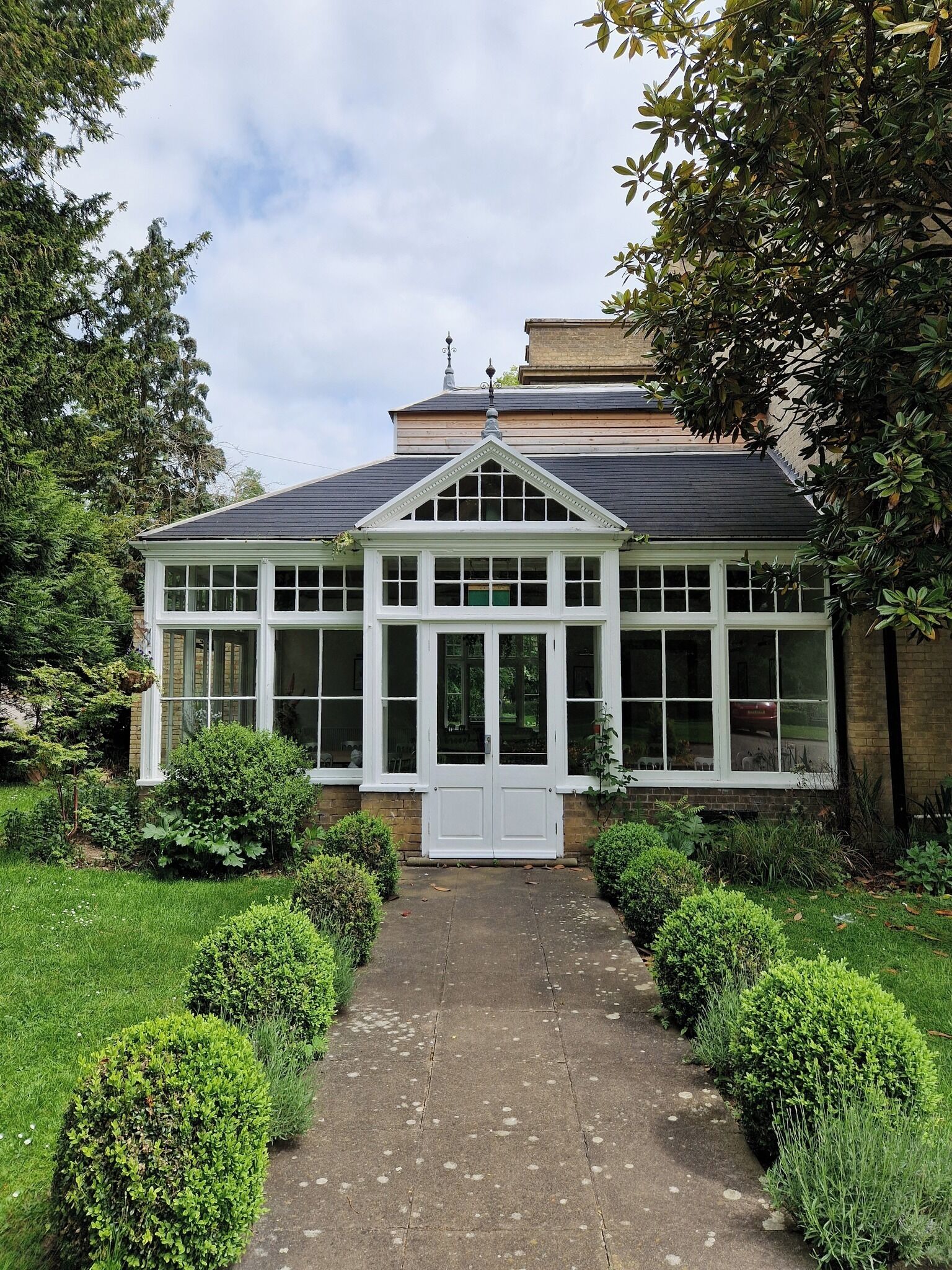 Ein traditionelles Haus mit symmetrischer Fassade, einem zentralen Eingang mit einer weißen Tür und einem Wintergarten mit zahlreichen Fenstern.