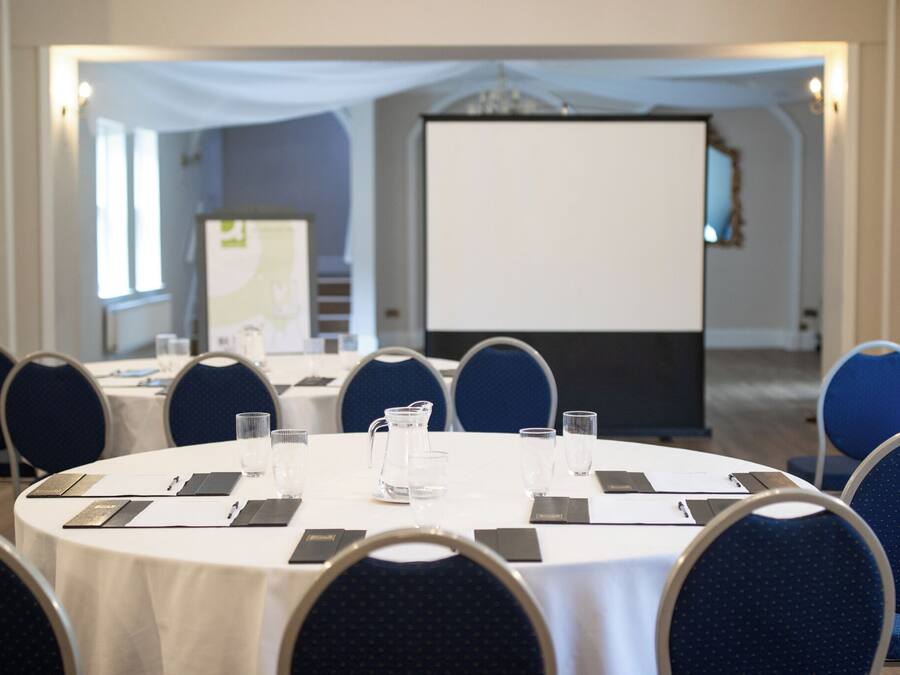 A conference room with round tables, chairs, and a projection screen.