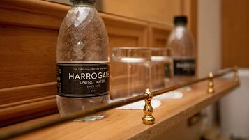 A Harrogate spring water bottle on a wooden shelf with glasses and a gold-colored handle.