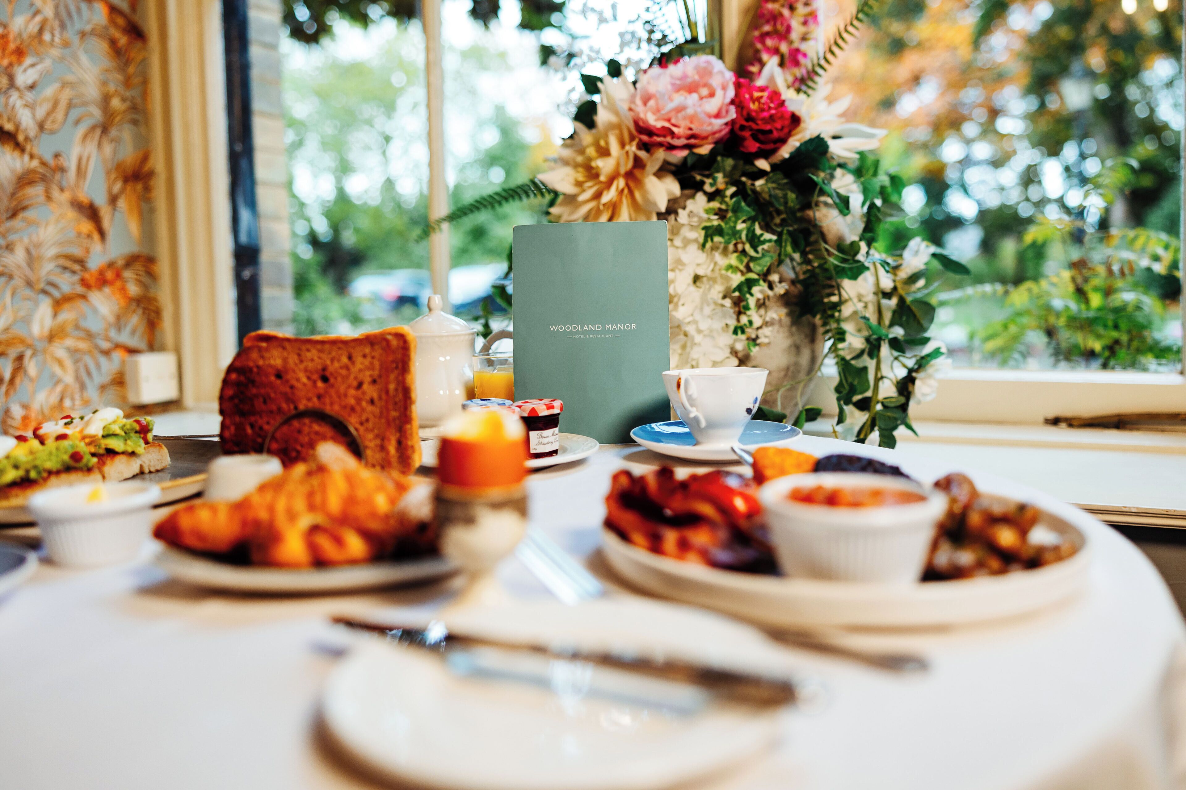 A breakfast table with various dishes, a menu, and a vase of flowers.