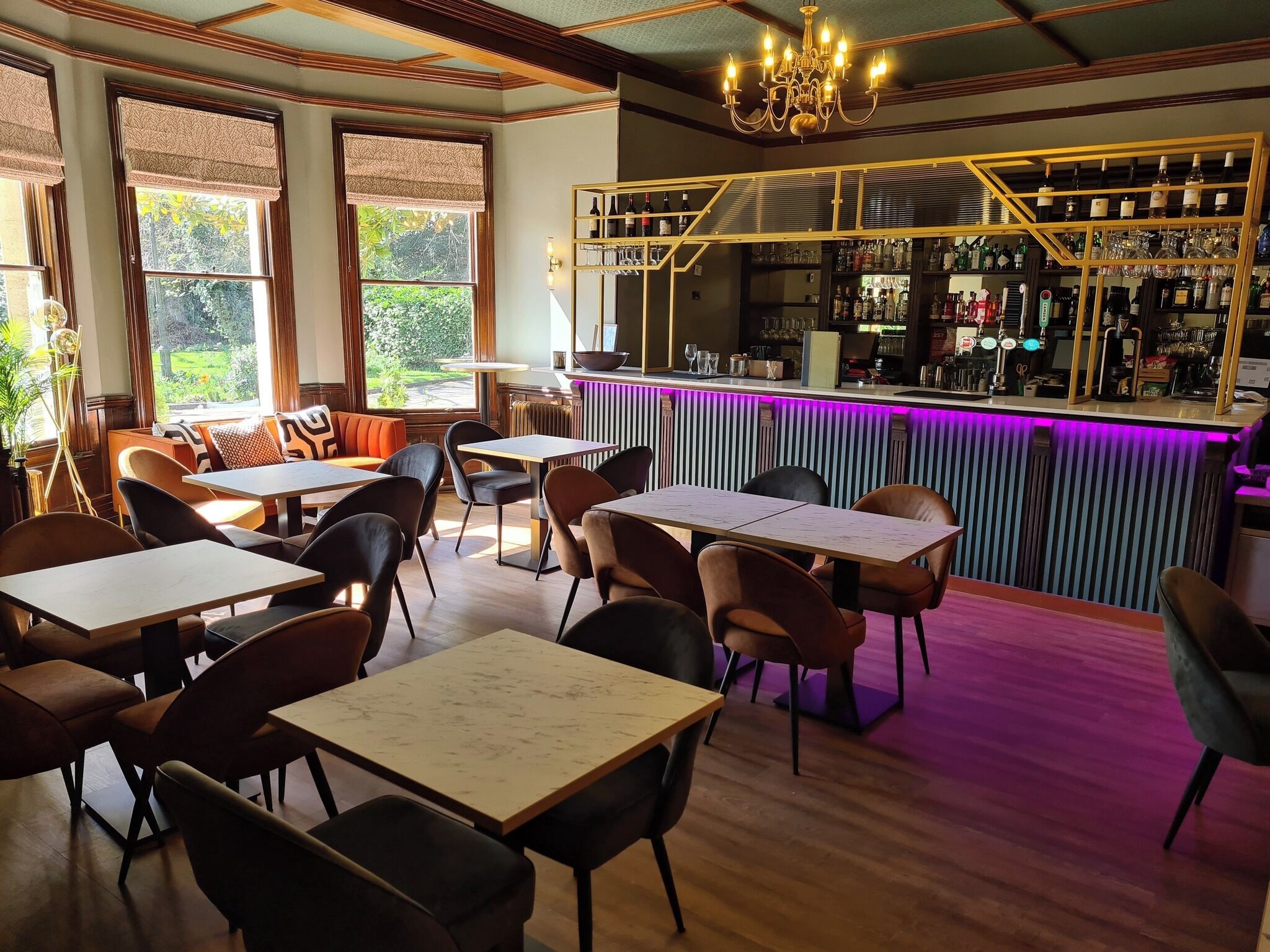 Un restaurante con barra, mesas, sillas y vistas al exterior con vegetación.