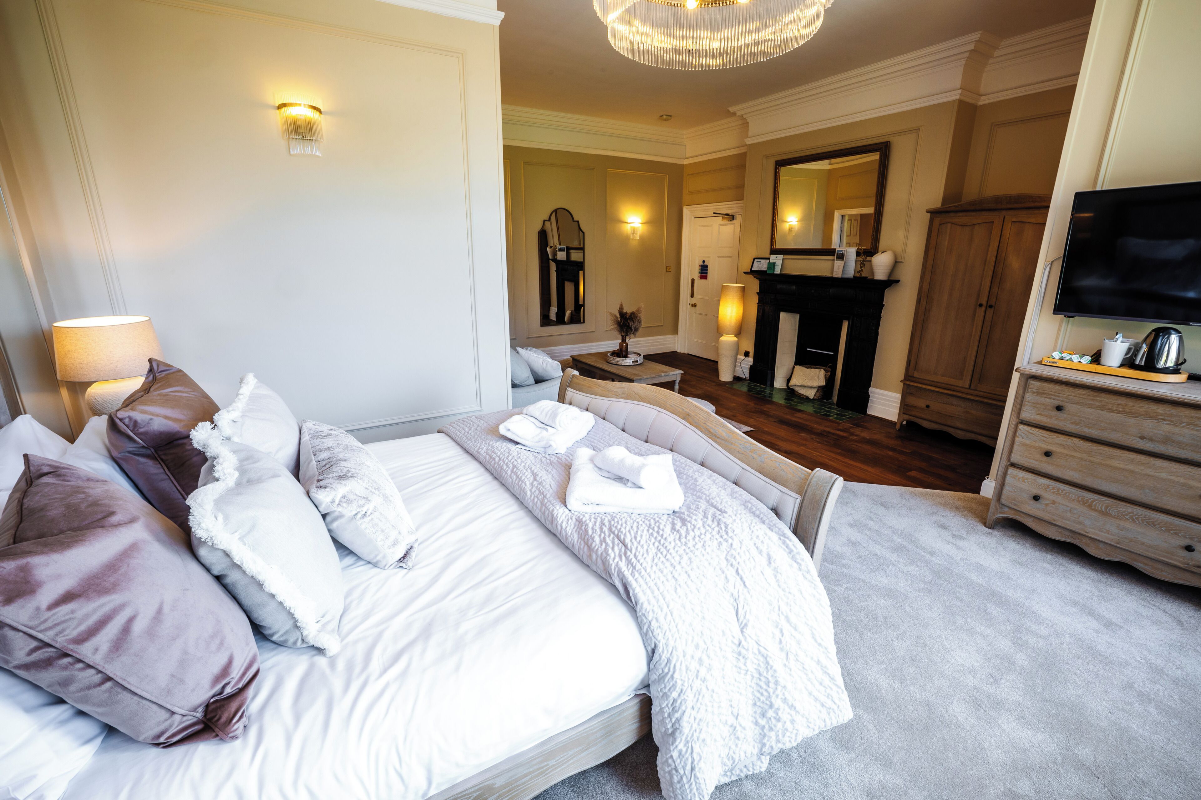 A hotel room with a bed, a television, a fireplace, and a mirror.