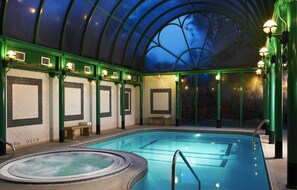Ein Hallenbad mit Glasdach, gefliesten Wänden und mehreren Leuchten.