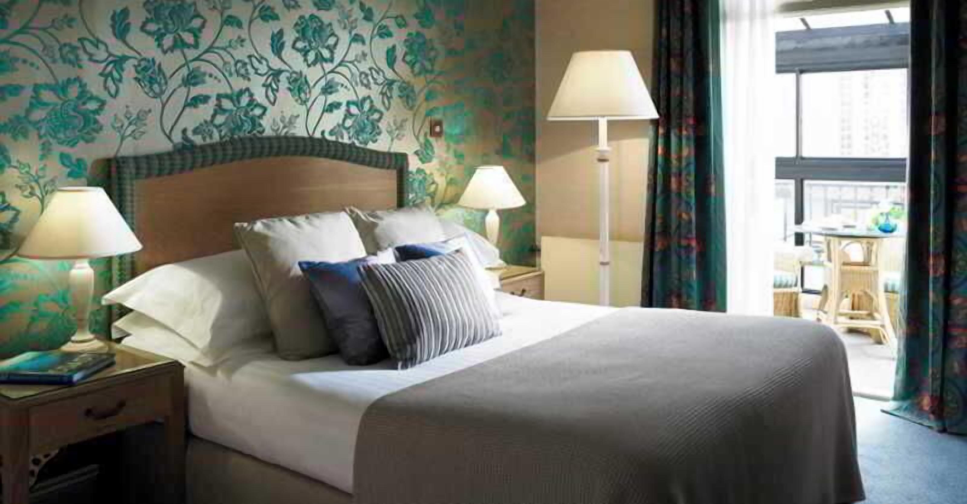 A hotel room with a bed, two bedside lamps, a nightstand, and a window with curtains.