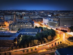Un paisaje urbano al atardecer con edificios históricos, un moderno edificio de vidrio y una concurrida intersección.
