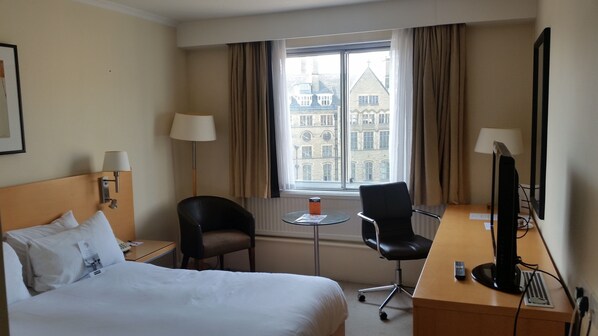 A hotel room with a bed, a desk with a computer, a chair, a small table, and a window with curtains. - The Bradford Hotel (Bradford)
