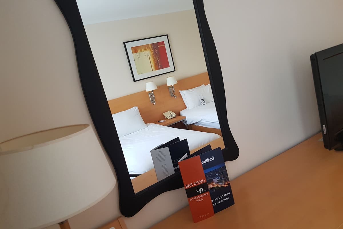 Une chambre d’hôtel avec un lit, une table de chevet, un téléphone et un tableau encadré au mur.