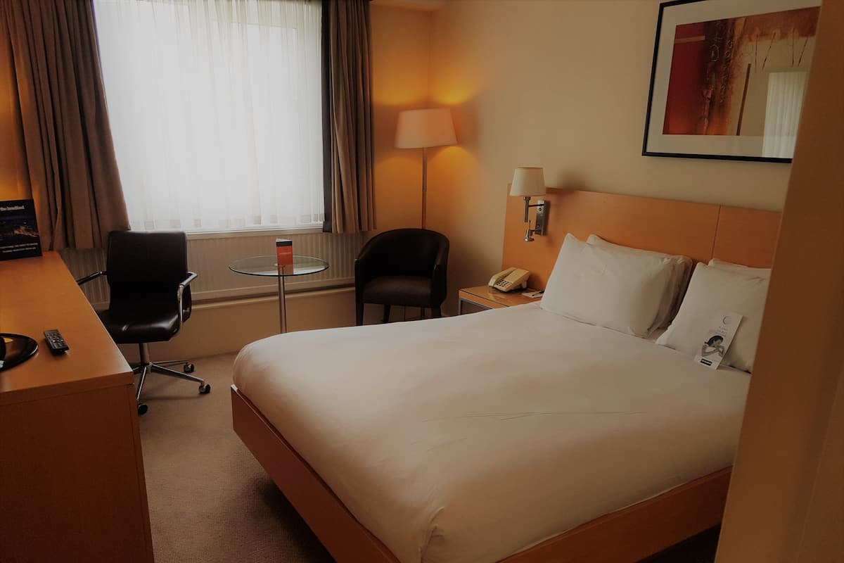 Une chambre d’hôtel avec un grand lit, un bureau avec une chaise, une petite table avec une lampe et un téléphone.